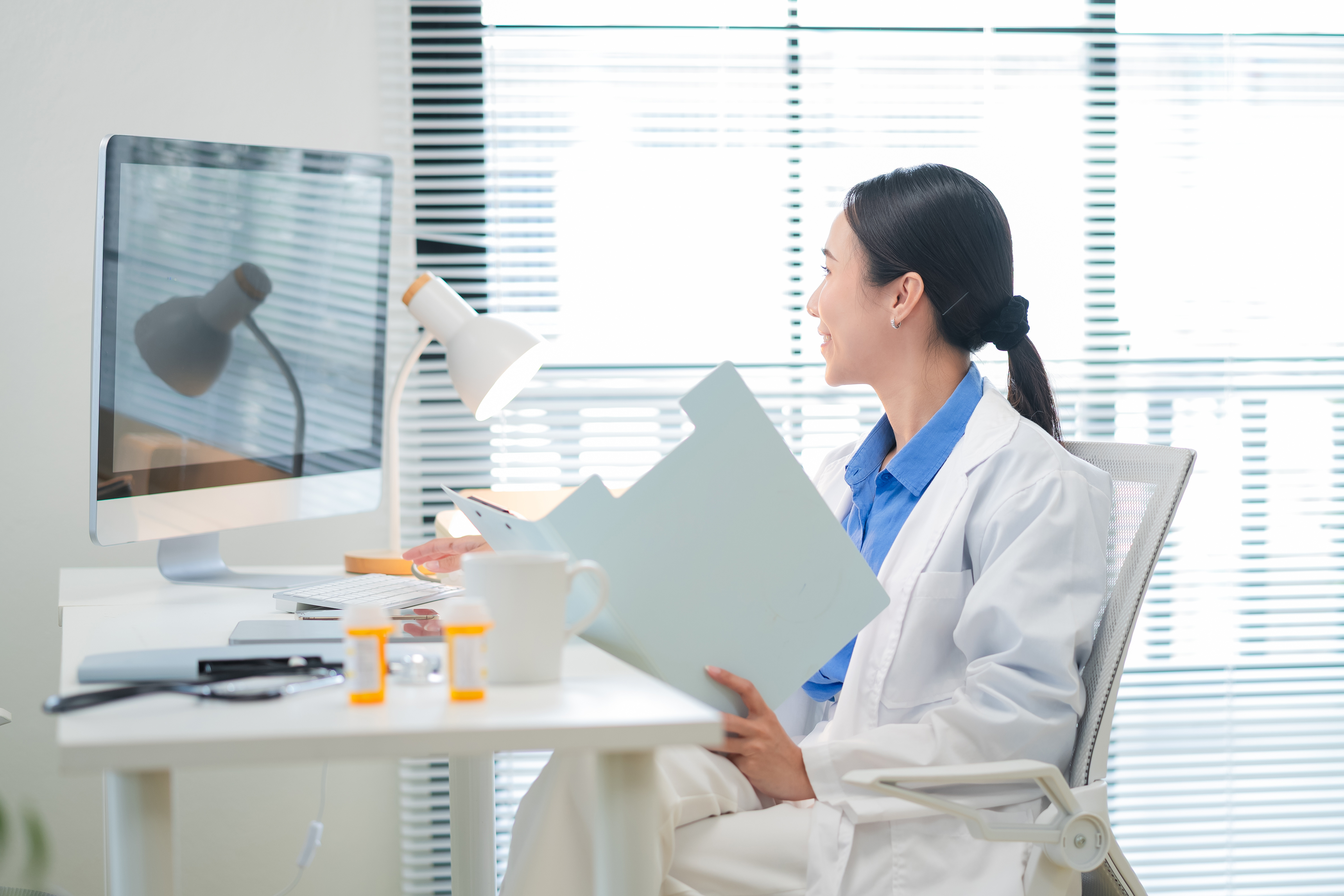 Physician reading a patient folder at a desktop computer